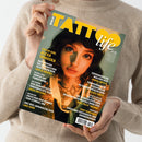 Person in beigem Strickpullover hält ein Magazin mit dem Titel „TATTOO life“. Auf dem Cover eine weiblich gelesene Person mit kurzem dunklem Haar, Nasenring und sichtbaren Hals-Tattoos vor grün-gelbem Hintergrund. Text auf dem Cover: „COVER GIRL ALEXA TAMASKA“, „FOTOGRAFISCHE MALEREI VON JANNA ANTICH“, „DAS NEO-JAPANISCHE VON UNO OWN“ sowie weitere Themen zu Tattoo-Kunst und Künstlern.