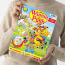 Helle, hellbraun gekleidete Person hält eine Kinderzeitschrift mit dem Titel „Disney Winnie Puuh“. Auf dem farbenfrohen Cover stehen die Figuren Winnie Puuh, Tigger, Rabbit und Ferkel auf einer grünen Wiese unter blauem Himmel. Unten sind runde grafische Elemente mit Aufschriften „Poster und Rätsel“ sowie „Naturforscher süßer Tiernachwuchs“ und Symbolen zu „Entdecken“, „Malen“ und „Spielen“ sichtbar.