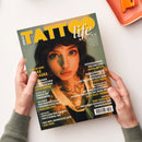 Titelbild der Zeitschrift „Tattoo Life“ mit großem gelbem Schriftzug und Untertitel „life“ in Weiß. Im Mittelpunkt eine weiblich gelesene Person mit braunen Haaren, Nasen- und Septumpiercing sowie sichtbaren Hals- und Brusttattoos, in goldgrünem Licht fotografiert. Um sie Textblöcke mit Artikelnamen und Autor*innen, unter anderem „Cover Girl Lexa Hlaska“, „Fotografische Malerei von Janna Antich“ und „Tattoo Shop Sinked Art London“.