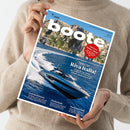 Eine Person in beigem Strickpullover hält das Magazin „boote“ Ausgabe 7/2026 vor neutralem Hintergrund. Auf dem Cover fährt eine dunkelblaue Motoryacht über blaues Meer vor einer felsigen Küste. Sichtbare Textelemente: Titel „boote“, Hauptüberschrift „Großer Test Riva Italia!“, Themenhinweise „Bootspflege“, „Gebrauchtboote“, „Niederlande“, „Seemannschaft“ und roter Kreis mit „7 Tipps für den Motor‑Check“.
