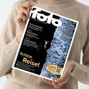 Person in beigem Strickpullover hält das Magazin „fotoMAGAZIN“ Ausgabe August 2026 in beiden Händen, Titelbild mit Luftaufnahme einer Person am Rand von schwarzem Felsen neben schäumender blauer Meeresoberfläche. Texte auf dem Cover: „Drohnenfotografie“, „Michael Kenna“, „Leichtes Gepäck“, „Schöne Reise!“, „Systemkameras“, „Smartphones“, sowie Hinweis auf Fotobuch-Aktion mit QR-Code unten rechts.