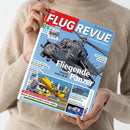 Eine Person in beigefarbenem Strickpullover hält das Magazin „FLUG REVUE – Das Luft- und Raumfahrt-Magazin“ mit rotem Kopfbereich und blauem Hintergrund, Titelthema „Fliegende Panzer – Ungarns letzte Mi-24“. Auf dem Cover sind ein grauer Kampfhubschrauber Mi-24 in Flugposition, ein gelbes Passagierflugzeug beim Start sowie kleinere Bildausschnitte zu Themen wie „US-Airlines in der Krise“ und „Zapfsäulen am Himmel“ zu sehen.