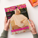 Titelblatt der Zeitschrift „InStyle“ mit großem pinkfarbenem Logo am oberen Rand. Auf dem Cover eine lächelnde hellhaarige Person in beigem Pullover und Shorts vor gelb-weiß gestreiftem Hintergrund. Textelemente: „EASY GLOWING – Die neuen Make-up-Looks“, „ACCESSOIRES FÜR HEISSE TAGE“, „PALM BEACH, SCHWEDEN, FLORENZ“ sowie „SOMMERHITS – Polka Dots Allover, Weiße Jeans, Süße Spitzen-Shorts, Coole Baseball-Shirts“. Hände halten das Heft über weißer Fläche.