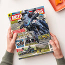 Titelbild der Zeitschrift „MOTORRAD NEWS“, Ausgabe August 2026. Im Mittelpunkt ein blau-weißes Motorradmodell Suzuki SV-7GX mit Fahrerin oder Fahrer in schwarzer Ausrüstung. Weitere kleinere Motorradabbildungen und Texte wie „Fahrbericht Suzuki SV-7GX“, „Szene-Reportagen“, „100 Jahre Ducati“ und „BMW S1000R“ auf farbigem Layout mit rot-gelben Überschriften und blauem Hintergrund, gehalten von zwei Händen über hellem Tisch.
