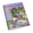 Titelbild der Zeitschrift „Wohnen & Garten“, Ausgabe Juli 2026. Im Zentrum ein sommerlich gedeckter Holztisch mit weißen Tellern, Gläsern, Besteck und Blumenarrangements in Blau, Weiß und Grün, Hintergrund mit Gartenambiente. Aufdrucke: „Blau-weiße Sommerträume“, „Dekorieren“, „Wohnen“, „Gastlichkeit“, „Garten & Pflanzen“, sowie „Staude des Jahres: Strahlende Schönaster“.