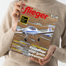 Person in beigem Pullover hält ein Exemplar des „flieger MAGAZIN“. Auf dem Cover fliegt ein weiß-blaues einmotoriges Flugzeug „Diamond DA20i Katana“ über eine Landschaft mit Wasserflächen. Textelemente: Titel „flieger MAGAZIN“, gelbes Feld mit „GO AROUND! So gelingt sicheres Durchstarten“, Artikelhinweise zu „Leserreise Frankreich“, „Medical-Tipps“ und „Turboprop-Einmot – Der Weg zum SET-Rating“.