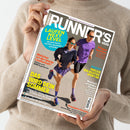 Person in beigefarbenem Strickpullover hält die Ausgabe des Laufmagazins „RUNNER’S WORLD“. Auf dem Cover laufen eine weibliche und eine männliche Person nebeneinander auf heller Asphaltfläche; beide tragen violette Sportkleidung und Sonnenbrillen. Sichtbare Schlagzeilen in farbigen Schriften lauten u. a.: „Laufen Next Level“, „Das wird dein Sommer“, „Welcher ist der beste Laufschuh?“, „Passt! Endlich der richtige Sport-BH“ und „Champion-Couple“.