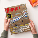 Titelseite des „flieger MAGAZIN“ mit großem rotem Schriftzug, darunter ein Foto eines einmotorigen weißen Flugzeugs Diamond DA20i Katana im Flug über einer Landschaft mit Wasserflächen. Schlagzeilen: „Neufauflage einer guten Bekannten“, „GO AROUND! So gelingt sicheres Durchstarten“, „Lesereise Frankreich“, „Medical-Tipps“ und „Turboprop-Einmot“. Gehalten von zwei Händen über hellem Tisch mit orangefarbenem Tablett.