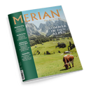 Magazin mit dem Titel „MERIAN – The Art of Travel“. Titelthema: „Sommer in den Alpen“, ergänzt durch Textzeilen „Wanderglück von Salzburg nach Triest“, „Im Salzkammergut“, „Eine große Runde durch die Schweiz“. Auf dem Cover grüne Wiesen mit braun-weißer Kuh im Vordergrund, verstreute Almhütten und Berge im Hintergrund. Linke Spalte in Grün mit Themenhinweisen zu Mexico City, Korfu, München und Teneriffa.
