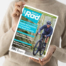 Titelblatt des Magazins „ElektroRad“ mit grün-blauem Layout; im Zentrum eine weibliche Person mit Helm, Sonnenbrille, dunkler Jacke und Shorts, die auf einem schwarzen Gravelbike auf einem Schotterweg fährt. Sichtbare Schlagzeilen u. a.: „Flotter auf Schotter – 11 Gravelbikes mit Spaß-Garantie“, „Der perfekte Sattel! Darauf kommt es an!“ und „Rushhour-Tipps vom Verkehrs-Experten“. Hände in beigem Pullover halten das Magazin.