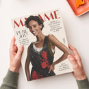 Titelseite des Magazins „MADAME“ mit einer lächelnden weiblichen Person mit kurzem, dunklem Haar im schwarzen Kleid mit roten Blumenmustern und olivfarbenen Trägern vor hellem Hintergrund. Text auf dem Cover: „PURE JOY! Die schönsten Aussichten auf die kommende Modesaison“, „REISE ZU DEN STERNEN – Zu Gast in den begehrtesten Hotel-Restaurants der Welt“ und „BEST OF DESIGN – Neue Möbel aus Mailand & Paris“. Zwei Hände halten das Heft.