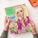 Magazincover „TOPModel by Depesche“ in buntem Design, mittig eine gezeichnete weibliche Figur mit hellblonden langen Haaren, rosa Pullover und Händen in Herzform; Titel in blauer Schrift auf grünem Hintergrund, umgeben von Texten wie „Knusper-Frühstück“, „Ein unvergesslicher Geburtstag“, „Happy Ostern“, „Stylecheck“ sowie QR-Code, kleinen Abbildungen und Sternmotiven, gehalten von zwei Händen über heller Oberfläche.