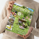 Person mit beigefarbenem Strickpullover hält das Magazin „LandIDEE“ in der Hand, Titelaufschrift „Land erleben und genießen“, Ausgabe Juli/August. Auf dem Cover sind ein sommerlicher Garten mit grüner Wiese, Holzzuber mit Wasser, Blüten und Kräutern sowie kleinere Gefäße mit Blumen zu sehen. Seitlich abgebildet: Fotos eingemachter Gläser, eines Insektenhotels und von Flaschen mit Öl und Kamillenblüten.