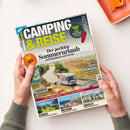 Titelbild des Magazins „Camping & Reise“ mit der Überschrift „Der perfekte Sommerurlaub in Deutschland und Europa“. Zentrale Abbildung eines Wohnmobils auf einer kurvigen Landstraße durch eine grüne Hügellandschaft, unten kleinere Fotos mit Landschaften aus Schweiz, Bretagne und Portugal. Weitere sichtbare Texte: „30 Tipps für Ihre Reise“, „Luxus-Reisemobile“, „Vorzelte“, „Kärnten entdecken“. Zwei Hände halten die Zeitschrift über hellem Tisch.