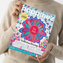 Eine Person in beigem Pullover hält das Magazin „happinez – Das Mindstyle Magazin“. Das Titelbild zeigt eine große, bunt gemusterte Blume mit der mittigen Aufschrift „Du bist“ und ringförmig angeordneten Worten wie „einzigartig“, „stark“, „geliebt“, „wertvoll“. Oben ein gelber Kreis mit dem Hinweis „EXTRA Wunderschönes Kraftbild zum Aufhängen“. Unten Textelemente: „Selbstachtung“, „Wie wichtig ist es, wirklich authentisch zu sein?“ sowie „Dossier Vom Glück enger Freundschaften“.