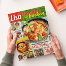 Titelblatt der Zeitschrift „Lisa kochen & backen“, Ausgabe August 2026, mit großem Foto eines Pasta-Gerichts mit Tomaten, Mozzarella und Basilikum auf grauem Teller. Textinhalte: „Neue Lieblingsrezepte! Mozzarella“, „Jetzt grillen: Fleisch, Fisch, Gemüse“, „Muffin-Träume“, „16 Seiten Spar-Rezepte“. Weitere kleine Bilder zeigen Zucchini-Gerichte, No-Bake-Kuchen und Ofenkartoffeln; gehalten von zwei Händen über hellem Untergrund.