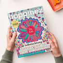 Titelbild des Magazins „happinez“, gehalten von zwei Händen über einer hellen Oberfläche mit orangefarbenem Tablett rechts oben; mittig farbenfrohes Mandala mit pink-, violett-, blau- und grünfarbigen Blütenblättern und der Aufschrift „Du bist“ im Zentrum sowie Worten wie „stark“, „besonders“, „einzigartig“; oben Logo „happinez – Das Mindstyle Magazin“, gelber Kreis mit Text „Extra Wunderschönes Kraftbild zum Aufhängen“, unten Schlagzeile „Selbstachtung“.