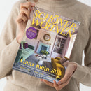 Helle Zeitschrift mit dem Titel „SCHÖNER WOHNEN – Europas größtes Wohnmagazin“, gehalten von einer Person in beigefarbenem Wollpullover. Auf dem Cover ist ein modern eingerichtetes Wohnzimmer mit grünem Sofa, gelbem Sessel, rundem Couchtisch und Kamin abgebildet. Sichtbare Schlagzeilen: „Ganz mein Stil“, „Ideen für Stadtgärten“, „Küchenliebe“, „Haus & Bauen“, „Neues Design“.