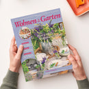 Titelbild der Zeitschrift „Wohnen & Garten“, Ausgabe Juli 2026. Auf dem Cover ein sommerlich gedeckter Holztisch mit Glasvasen, blau-weißen Blumen, Tellern, Gläsern und Besteck im Freien. Überschriften: „Blau-weiße Sommerträume“, „Dekorieren – Rundsukkulenten als kreativer Blickfang“, „Wohnen – Leicht einrichten wie im Urlaub am Meer“, „Gastlichkeit – Wir dekorieren und kochen mit Süßlupinen“. In menschlichen Händen gehalten, neutraler Hintergrund.