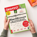 Titelblatt der Zeitschrift „ÖKO-TEST“ Ausgabe Juli 2023 mit grün-rotem Randdesign, gezeigt in den Händen einer Person vor hellem Hintergrund. Haupttitel: „Mineralwasser – Wie rein ist Ihr Sprudel? 56 Medium-Produkte im Test“. Weitere sichtbare Texte: „LUXUSGUT WASSER“, „TEST 182 PRODUKTE FÜR JEDEN TAG“, „EXTRA SCHULSTART“, „KLEBESTIFTE IM TEST“. Oben rechts Porträt eines Mannes mit Brille im Interviewfeld.