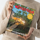 Beige gekleidete Person hält eine Ausgabe der Zeitschrift „Das Haus“ mit rotem Titel auf hellblauem Hintergrund. Titelthemen u. a.: „Erdwärmekörbe: Viel Energie trotz wenig Fläche“, „Überraschend schön – 60er-Jahre-Wohnung im Grünen“ und gelber Kreis mit Text „Einrichten: Kleinen bis großen Kinder­möbeln, diese wachsen mit“. Cover zeigt beleuchtetes Haus mit Treppe und Terrasse im Grünen in der Dämmerung.