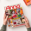 Aufgeschlagenes Handarbeitsmagazin „Anna“ in zwei Händen auf weißer Fläche, mit zwei gehäkelten Igel-Figuren in rotem Kleid und grüner Hose auf dem Titelbild. Sichtbare Texte: „Ideen zum Selbermachen • Kreativ und aktuell“, „Die schönsten Handarbeits-Ideen“, „Herbstglück für dich & mich“ und „Lehrgang: Handschuhe stricken in Reihen“; oben rechts liegt ein orangefarbenes Bürogerät.