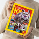 Person in beigefarbenem Strickpullover hält eine Ausgabe des Magazins „National Geographic Kids“ mit gelbem Rand und rotem Titel. Auf dem Cover ist eine große Eule mit weit geöffneten Augen abgebildet. Text: „EULEN: Mit großen Augen durch die Nacht!“, daneben kleinere Themenfelder zu „Orcas“, „Pharaonen“ und „Dinosaurier“ sowie der Hinweis „2 starke Poster!“.