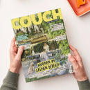 Titelblatt der Wohnzeitschrift „COUCH“ mit gelbem Schriftzug und Untertitel „Alles, was du liebst“. Abgebildet ist eine Frau in heller Kleidung an einem weiß gedeckten Gartentisch unter einer grünen Laube mit Hängeblüten, daneben ein heller Hund auf Steinboden. Texte auf dem Cover: „Wohnen im grünen Bereich“, „Besser schlafen“, „Gartenglück“, „Farbtrend Rosabi“ und „Festival-ABC“. Hände halten das Magazin über hellem Tisch mit orangefarbener Ablage.