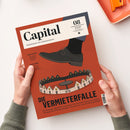 Rot-orange Ausgabe des Wirtschaftsmagazins „Capital“, schräg von oben auf weißem Untergrund fotografiert und von zwei Händen gehalten. Das Cover zeigt eine schwarze Lederschnürschuh-Illustration über einem kreisförmigen Häuserensemble sowie die Texte „WIRTSCHAFT IST GESELLSCHAFT“, „CHINA-GEFAHR – Die große Warenflut kommt“, „AKTIVE FONDS“ und „DIE VERMIETERFALLE“.