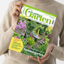 Person in beigefarbenem Strickpullover hält das Magazin „mein schöner Garten“ (Ausgabe Juni 2025) in beiden Händen, Titel in Grün-Weiß mit Unterzeile „Europas größtes Gartenmagazin“. Auf dem Cover ein sommerlicher Garten mit blühenden Stauden, grünem Laub, Holztisch und Stühlen. Sichtbare Texte: „Richtig düngen leicht gemacht“, „Unsere 50 schönsten Ideen für Ihren Sommergarten“, „Gartenpraxis im Juni“, „Exotisches: Wassermelonen anbauen und ernten“.