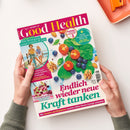 Titelbild der Zeitschrift „Good Health“, Ausgabe Nr. 6 Juli/August 2023. Zentrale Bildfläche mit Spinatblättern, Tomatenscheiben, Blaubeeren, Walnüssen und Mandeln. Überschriften: „Endlich wieder neue Kraft tanken“, „Wie Bewegung unser Gehirn fit hält“, „Squats formen Bauch, Beine, Po“, „Für Immunsystem und Tiefschlaf – Die Super-Power der Kirschen“. Zwei Hände halten das Magazin vor hellem Hintergrund.