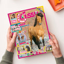 Titelbild der Kinderzeitschrift „Lissy“ mit großem Foto eines braunen Pferdes auf steinigem Untergrund im Zentrum. Mehrere bunte Textfelder mit Aufschriften wie „Coole Punkte Appaloosa“, „Fotoroman – Lola in Gefahr“, „2 bezaubernde Poster!“ und „Teste dein Lissy-Wissen!“ sowie kleinen Abbildungen von Pferden und Comicfiguren auf pinkem Randdesign; gehalten von zwei Händen vor hellem Hintergrund.