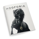 Magazin mit dem Titel „HOOFORIA“ in schwarzer Schrift auf weißem Hintergrund, darunter der Text „NACHDENKEN · BEWEGEN · VERSTEHEN · BEGEISTERN“. Auf dem Cover zentral ein schwarzes Pferd mit wehendem Schweif und Mähne, realistisch fotografiert, unten das goldfarbene Logo „HC“ und die Aufschrift „VOLUME I“. Perspektive leicht schräg von oben auf das geschlossene, glänzende Magazin.