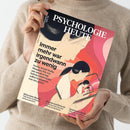 Person in beigefarbenem Strickpullover hält die August-2023-Ausgabe der Zeitschrift „Psychologie Heute“ in beiden Händen. Das Cover zeigt eine grafische Illustration mehrerer Personen mit dunklem Haar und Smartphone vor einem Hintergrund aus geschwungenen Rot‑, Rosa‑ und Beigetönen. Titeltext: „Immer mehr war irgendwann zu wenig“, dazu Unterzeilen zu Themen wie Serien, Social Media, Konsum, Achtsamkeit und Psychologie.