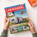 Titelbild des Magazins „CARAVANING – Europas großes Camping-Magazin“, Ausgabe Juni 2025. Rotes Titelband mit weißer Schrift, darunter Foto einer Familie mit zwei Kindern neben einem weißen Wohnwagen der Marke Dethleffs auf einer grünen Wiese. Textelemente: „Dethleffs Camper 560 FMK“, „Exklusiv: Neue Eriba-Modelle“, „Feeling und Novaline“, „Atlantikküste“, „Gadgets für Camper“. Hände halten das Magazin über weißem Tisch mit orangefarbenem Tablett.