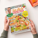 Titelbild der Gesundheitszeitschrift „Iss dich GESUND – Besser leben mit Genuss“, herausgegeben von Dr. Matthias Riedl, mit Foto eines Mannes in grünem Hemd und einer Gemüse-Pizza mit Basilikumblättern auf Holzbrett. Sichtbare Schlagzeilen: „Die Super-Kraft der Ballaststoffe“, „Das beste Essen fürs Herz“, „Ernährungs-Doc für zu Hause“ und „Adipositas – Wie Mario 45 Kilo abnahm“. Zwei Hände halten das Magazin über hellem Hintergrund.