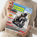 Titelblatt der Motorradzeitschrift „Tourenfahrer“ mit großem gelbem Schriftzug auf blauem Hintergrund. Im Mittelpunkt fährt eine Person in brauner Schutzkleidung und schwarzem Helm auf einem weißen Motorrad mit rotem Streifen auf einer kurvigen Bergstraße. Seitlich sind Schlagzeilen zu Themen wie „SENIORENSPORT“, „ASIA-TWINS“, „HOCHGENUSS“ und „ALLZWECK IN ELEGANZ“ in weißen, roten und gelben Schriftfeldern angeordnet.