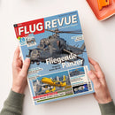 Titelblatt des Magazins „FLUG REVUE“ mit großem Foto eines grauen Militärhubschraubers vom Typ Mi-24 im Flug über blauem Himmel. Hauptüberschrift: „Fliegende Panzer – Ungarns letzte Mi-24“. Weitere Texte: „US-Airlines in der Krise“, „Neue Jets und Hubschrauber für die Bundeswehr“, „ZAPFSÄULEN AM HIMMEL“ und „RENNENERGIE IM ALL“. Gehalten von zwei Händen über weißer Tischfläche mit orangefarbener Schale oben rechts.