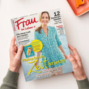 Titelbild der Zeitschrift „Frau im Leben“ Juli 2026 mit einer lächelnden Frau in türkis gemustertem Sommerkleid am Meer. Hauptüberschrift in Gelb: „Meine beste Zeit ist jetzt!“, weitere Texte u. a. „Die neue Lust am Fasten“, „12 Sommerkleider – Mode für heiße Tage“, „Radeln & Baden“, „Sommer-Spezial: Taschenbücher für den Urlaub + Rätsel & Knobelspiele“. Zwei Hände halten die Zeitschrift über hellem Hintergrund.