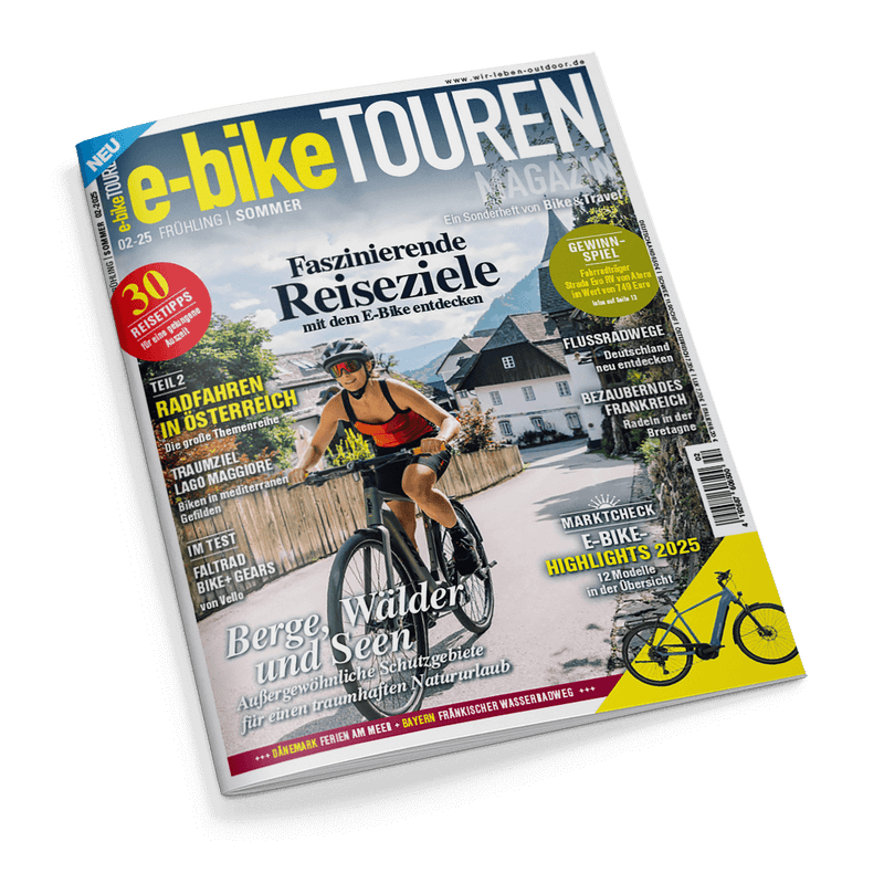 Cover des Magazins e-bike TOUREN, Ausgabe Frühling/Sommer 02-25, zeigt eine lächelnde Person auf einem E-Bike in einem Dorf mit der Schlagzeile Faszinierende Reiseziele mit dem E-Bike entdecken.