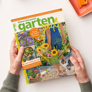 Schräg gehaltenes, glänzendes Gartenmagazin „garten spaß“, Ausgabe September 2026, mit grün-gelbem Logo, orangefarbener Kopfzeile „Das Garten-Magazin mit vielen Schritt-für-Schritt-Anleitungen“ und dem Titel „Gärtnern leicht gemacht“. Das Cover zeigt eine Person im Garten, Sonnenblumen, weitere Blumen, eine Gießkanne, eine Katze und mehrere kleinere Bildfelder mit Texten wie „Trends für Topf & Terrasse“ und „Volle Kanne Spätsommer“; zwei Hände halten das Magazin vor weißem Hintergrund.