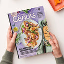 Magazin „Lust auf Genuss“ mit violettem Cover, gehalten von zwei Händen. Sichtbare Texte: „BONJOUR PROVENCE“, „Von Ratatouille über Quiche bis Tarte au citron“ und „DAS BESTE AUS SÜDFRANKREICH“; abgebildet sind ein Teller mit gebratenem Geflügel, Gemüse und Kräutern, Brot, Artischocken, Lavendel sowie Besteck und ein orangefarbenes Tablett im Hintergrund.