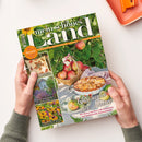 Zeitschrift „mein schönes land“, schräg auf weißem Untergrund von zwei Händen gehalten. Das Cover zeigt grüne Blätter, Sonnenblumen, Äpfel im Weidenkorb, einen Apfelkuchen und Gartenmotive; sichtbare Texte: „Gutes bewahren · Schönes entdecken“, „30 Seiten kreativ durch den Herbst“, „Geschenke der Natur“, „Bunter Blütenzauber im Landhausgarten“ und „Sonnenbraut pflanzen, kombinieren & pflegen“.