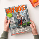 Magazinecover „BIKE“ mit orangefarbener Titelzeile „RAD & E-BIKE • TECHNIK • REISEN“ und männlicher Person auf einem roten Fahrrad vor Hochhäusern. Sichtbare Texte: „BLINKER AM FAHRRAD – PRAXIS-CHECK & RECHTSLAGE“, „NEWCOMER AVENTON“, „Specialized Vado 3X Test Suite 36“, „TOURENRÄDER UNTER 1800 EURO“ und „DIAMANT, DECATHLON & STEVENS IM TEST“.