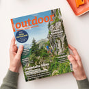 Outdoor-Magazin „outdoor“ mit orangefarbener Titelschrift und dem Untertitel „WANDERN. REISEN. ABENTEUER.“; das Cover zeigt eine alpine Felslandschaft mit zwei wandernden Personen und wird von zwei Händen gehalten. Sichtbare Texte: „Japan – Wanderjuwel“, „Traumhafte Alpen“, „Kochen & Genießen“, „Rucksäcke“ sowie „Friaul-Julisch Venetien: Paradies zwischen Meer & Bergen“.