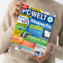 Hochkantaufnahme einer weiblichen Person ohne sichtbares Gesicht, die ein schräg gehaltenes, glänzendes PC-Magazin mit blau-gelbem Cover in beiden Händen hält. Lesbare Texte: „PC WELT plus“, „2 DOPPEL-DVDs +32 SEITEN EXTRA“, „Windows Pro gratis!“, „Update mit 1-Klick“, „Ihr Recht auf Reparatur“ und „WLAN-Tuning“; beige Strickkleidung im Hintergrund.