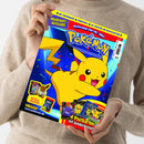 Eine weibliche Person im beigen Strickpullover hält schräg eine glänzend bedruckte Pokémon-Zeitschrift mit gelbem Pikachu, blauem Hintergrund und buntem Konfetti. Sichtbare Texte: „3D-Anhänger“, „FunPack“, „XL-Poster“, „Postkarten“, „Highlight-Ausgabe“, „Schnapp sie dir alle!“, „Pokémon“, „Mit Mega-Gewinnspiel!“, „4 Postkarten mit Goldprägung!“, „Panini“ und „www.pokemon.de“.