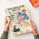 Zeitschrift „PSYCHOLOGIE HEUTE“ mit cremefarbenem Cover, gehalten von zwei Händen. Eine Illustration zeigt zwei weibliche Figuren in blauer und grüner Kleidung; lesbare Texte: „Konflikte leichter lösen“, „ADHS und Autismus – Ein Leben zwischen zwei Extremen“, „Abnehmen – Verändert es die Liebe?“ und „Arbeitsweg – Kreative Lösungen gegen Stress“.