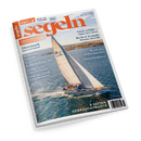 Schräg liegendes Hochglanzmagazin „segeln“ mit weißem Rand auf schwarzem Hintergrund. Das Cover zeigt ein weißes Segelboot mit großen beigen Segeln auf blauem Wasser vor einer Küstenlandschaft; sichtbare Texte: „Juli/August 2026“, „Fahrten- und Freizeitsegeln“, „Dänemark – Fünen und Seeland“, „Recht & Technik“ und „8 SEITEN GEBRAUCHTBOOTE“.