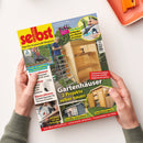 Aufgeschlagenes DIY-Magazin „selbst ist der Mann – Das Do-it-yourself-Magazin“, schräg von oben von zwei Händen gehalten. Das Cover zeigt ein hölzernes Gartenhaus, eine Person auf einer Leiter, Werkzeuge und Themen wie „Gartenhäuser: 2 Projekte selber bauen“, „Anti-Rost: Geländer aus Metall streichen“, „Laub-Sauger im Praxistest“ und „Großes Saunahaus“.